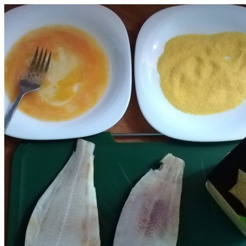 1. Этап. Жареная камбала в хрустящей панировке: Камбалу чистим, отрезаем голову и плавники. Я отрезаю всегда кухонными ножницами. Моем тщательно. При чистке небольших тушек камбалы шкурку, как правило, оставляют. Лишь убирают чешую и шипы. В одну тарелку разбила яйцо и посолила его, немного подвзбила. В другую тарелку выложила кукурузную поленту ТМ BRAVOLLI.