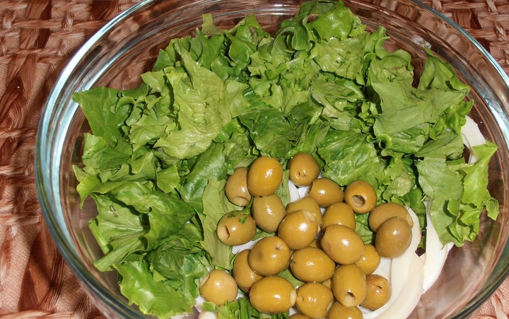 1. Этап. Новогодний салат из кальмаров: Листья салата промойте и порвите руками, добавьте к кальмарам. Также кладем оливки.