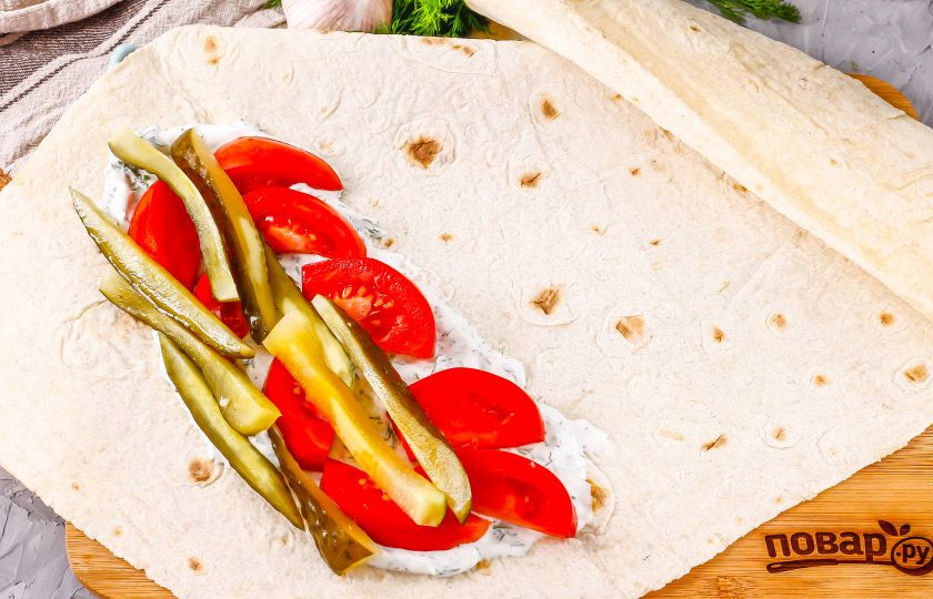 1. Этап. Азербайджанская шаурма: Смажьте половиной соуса край тонкого армянского лаваша, выложите на него нарезанные помидоры и огурец.