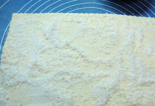 1. Этап. Творожное печенье с кокосовой стружкой: Тесто разделить на несколько частей. Одну часть раскатать в пласт примерно размером 25см на 15см. Если необходимо, то добавьте муки при раскатке. Посыпьте сахаром и кокосовой стружкой.