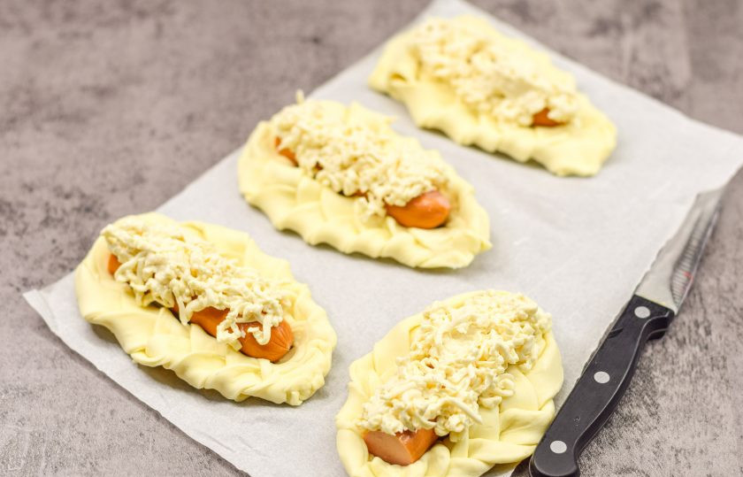 1. Этап. Плетеные Хот-доги из слоеного теста с плавленым сыром: Поверх сосисок выложите натертый плавленый сыр.