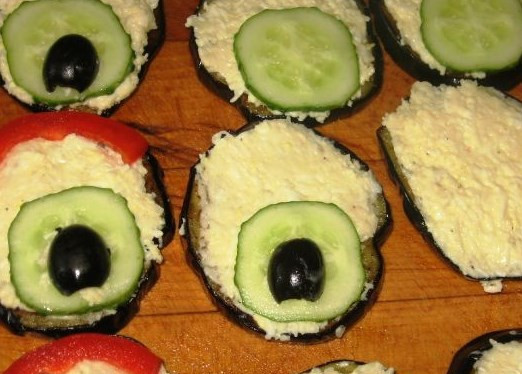 1. Этап. Баклажаны жареные Павлиний хвост: Каждый кружок баклажана намажем салатной массой. На один конец кружка выложим кружочек огурца и сверху уложим половинку маслины. На противоположный конец выкладываем по самому краю полоску перца.