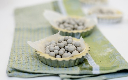 1. Этап. Тарталетки с голубикой: Выложите тесто в формочке, предварительно смазанные маслом и застеленные бумагой для выпечки. В тесто положите груз, хорошо для этого подходят сухие бобовые (фасоль, горох). Запекайте примерно 10-15 минут в духовке, разогретой до 200 градусов.