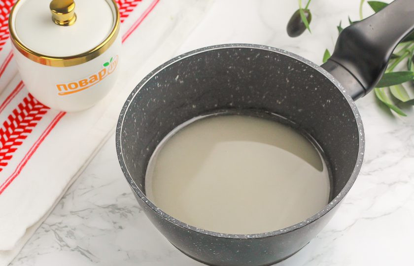 1. Этап. Зефир из яблок: Всыпьте сахарный песок в казан или кастрюлю, ковш с антипригарным толстым дном. Влейте воду, перемешайте и поместите на плиту, включая средний нагрев.