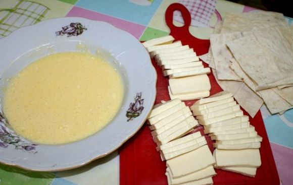 1. Этап. Конверты из лаваша с сыром: 2. Также нужно нарезать тонкими пластинками сыр. При желании в рецепт приготовления конвертов из лаваша с сыром можно использовать бутербродный плавленый сырок с различными добавками. Для кляра необходимо взбить в небольшой мисочке яйца, добавить соль по вкусу и крахмал.