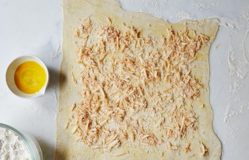 1. Этап. Сырные палочки из слоеного теста: Шаг 2. Раскатайте слоеное тесто, присыпьте его 1/3 частью натертого сыра.