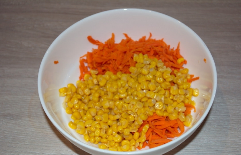 1. Этап. Салат с кукурузой консервированной: Поместите морковь в емкость. Теперь вскройте банку с кукурузой. Добавьте кукурузу в салатник к моркови.