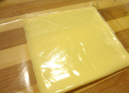 1. Этап. Плавленый сыр с начинкой: Берем ломтик плавленного сыра и вскрываем упаковку, но не освобождаем сыр от нее. С упаковкой нам будет легче завернуть сыр с начинкой.