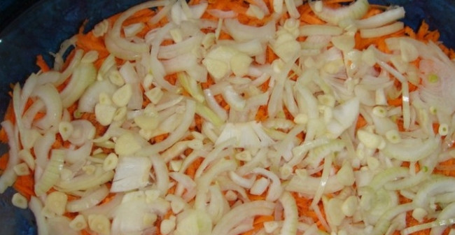 1. Этап. Рыба пангасиус в духовке: 2. Чищу и мою лук, нарезаю его тонкими полукольцами. Зубчики чеснока чищу и нарезаю кольцами. Укладываю лук с чесноком поверх моркови.