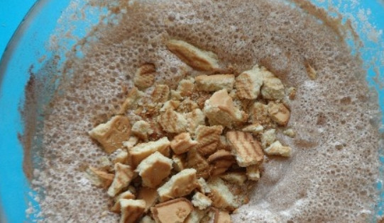 1. Этап. Шоколадный манник: Теперь кладем какао и растопленное сливочное масло. Взбиваем венчиком и добавляем соду, гашенную уксусом и раскрошенное печенье. Перемешиваем.