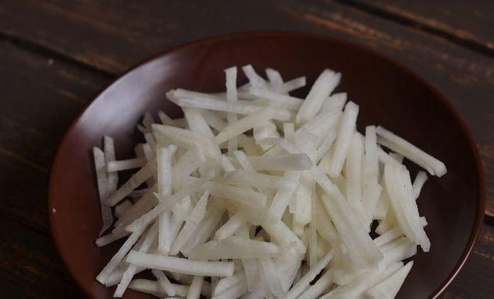 1. Этап. Легкий мясной салат: Очистите и вымойте дайкон. Нарежьте его тонкой соломкой. Вместо дайкона, если его нет под рукой, можно использовать любые сочные и свежие овощи на ваш вкус.