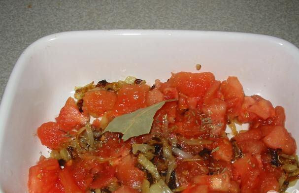 1. Этап. Тунец в томатном соусе: 4. Когда приготовится лук, его выложить на дно огнеупорной формы, приправить солью и перцем, сверху выложить помидоры. Сверху положить чеснок, тмин и лавровый лист и положить в духовку на 20 минут при температуре 160 градусов.