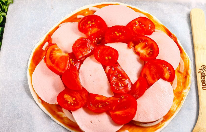 1. Этап. Пицца с колбасой из слоеного теста: Промойте помидоры и нарежьте их слайсами, вырезая зеленые сердцевинки. Выложите на основу.