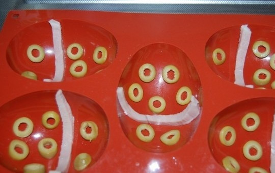 1. Этап. Закуска Пасхальные яйца: 5. Зеленые оливки нарежьте тонкими кольцами, ветчину — на полоски. Уложите их в силиконовые формочки, как на фото.