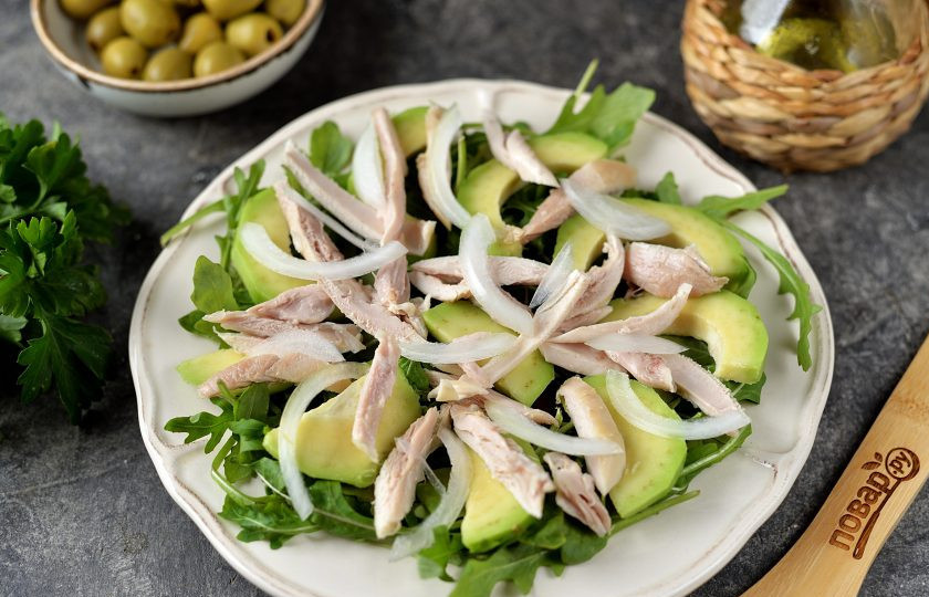 1. Этап. Салат с курицей, авокадо и рукколой: Отделите куриное мясо от костей, нарежьте его тонко или порвите руками на волокна, выложите на авокадо, посыпьте все белым луком, нарезанным полукольцами.