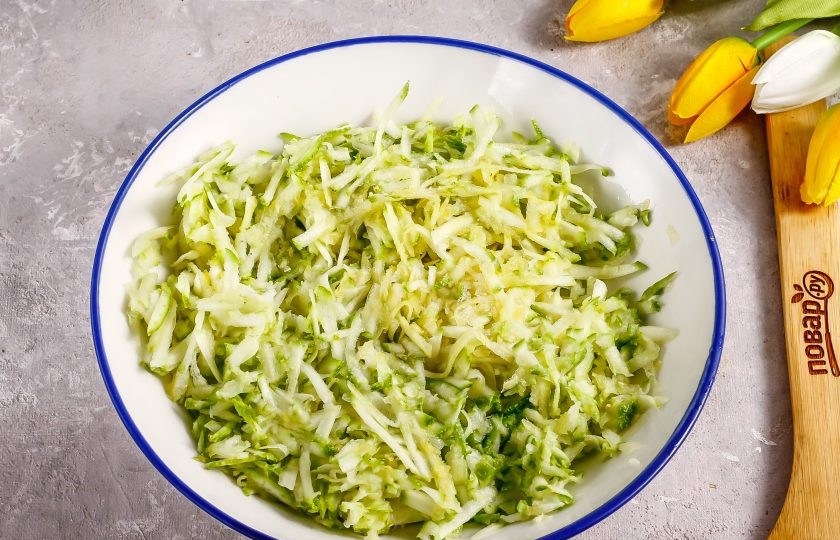 1. Этап. Оладьи из кабачков с бананом: Кабачок промойте в воде, срежьте хвостики с овоща и натрите на терке с крупными ячейками в глубокую емкость. Посолите и оставьте на 5 минут, чтобы нарезка выделила жидкость. Затем отожмите всю жидкость.