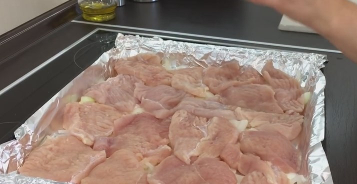 1. Этап. Куриная грудка под кабачками: 2. Мясо нарежьте пластами и отбейте молотком. Выложите всё на лук, посолите или сбрызните соевым соусом, поперчите.