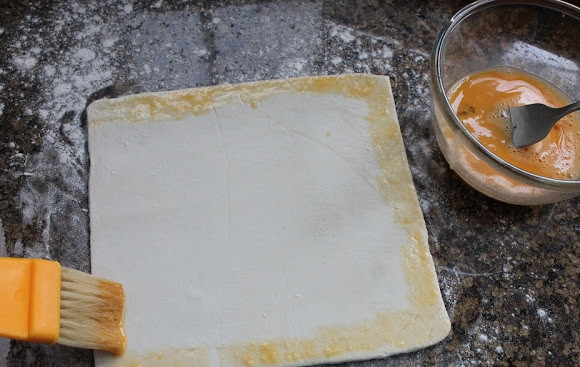 1. Этап. Пирожки с сюрпризом: 6. Раскатайте слоеное тесто, нарежьте квадратиками. Края смажьте взбитым яйцом.