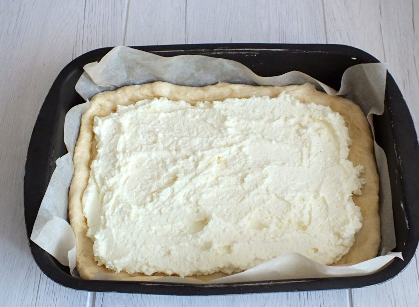 1. Этап. Татарский пирог с творогом: Возьмите противень или форму для выпечки. Застелите бумагой или смажьте маслом. Переложите в форму большой пласт теста. На него выложите начинку из творога, оставляя небольшое расстояние с краёв.