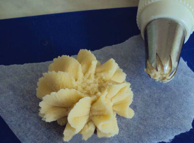 1. Этап. Курабье по ГОСТу: Для выпекания необходим кондитерский мешок. Вручную сформировать такие печеньки вам не удастся. Возьмите звездчатую насадку. Постелите на противень пергаментную бумагу. Выдавите кондитерским мешком небольшого размера печенья. В середине каждого сделайте пальцем углубление. Оно может быть побольше и поменьше, в зависимости от того, сколько вы будете класть варенья.