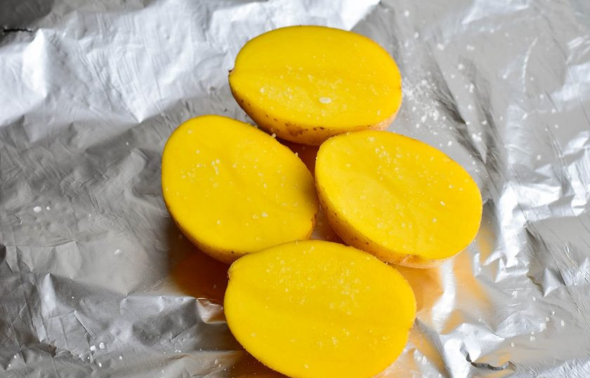 1. Этап. Крабовый салат как в Крошке-картошке: Вымойте картофель, разрежьте его пополам и выложите на фольгу. Посолите овощи.