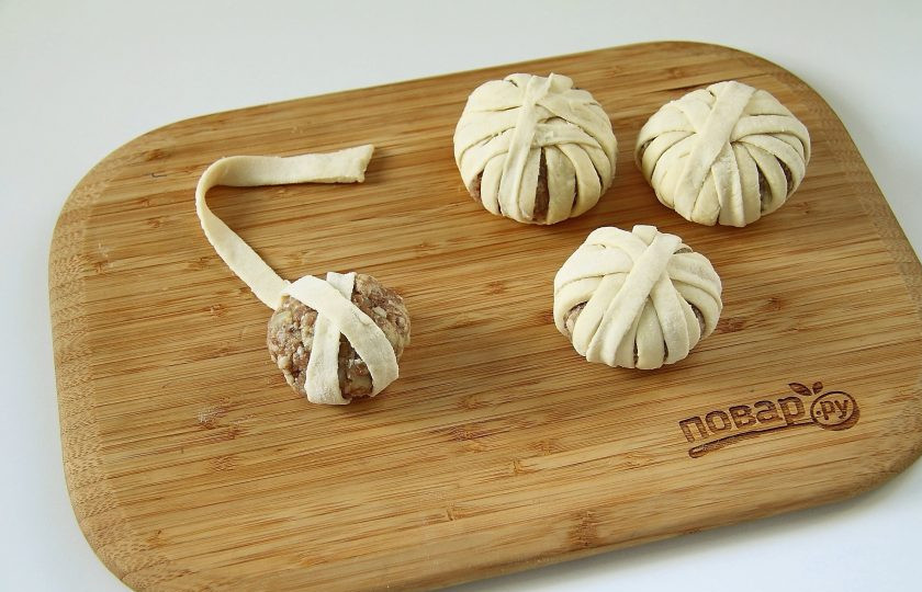 1. Этап. Мясные шарики в слоеном тесте: Из фарша слепите шарики и обмотайте их полосками теста по окружности клубочком, примерно по 2-3 полоски на каждый шарик.