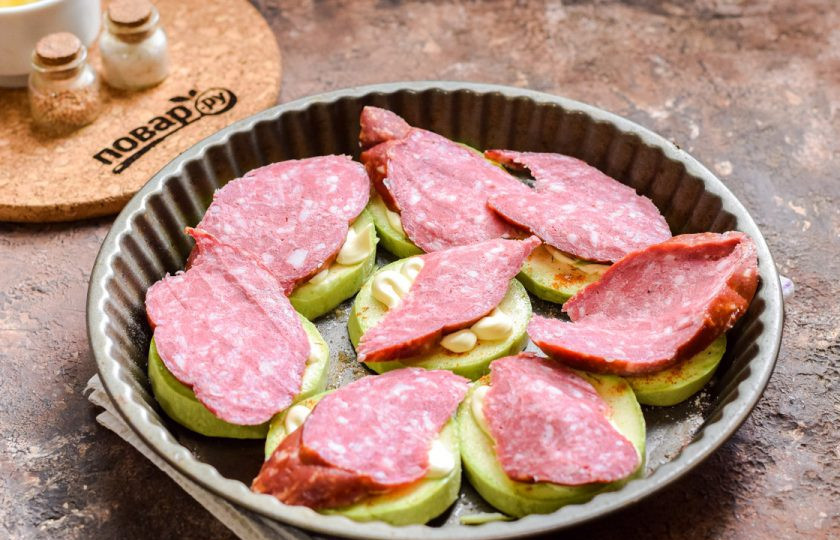 1. Этап. Кабачки под шубой в духовке: Колбасу выбирайте самую вкусную. Нарежьте колбасу щедрыми кусочками и выложите поверх кабачков. Для диетического варианта используйте сметану и вареное куриное филе.
