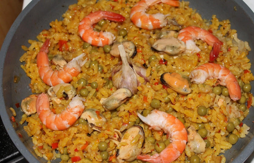 1. Этап. Паэлья маринара: Через 10 минут выкладываю к рису морепродукты, горошек, втыкаю в серединку неочищенную головку чеснока и подливаю бульона. Готовлю на медленном огне