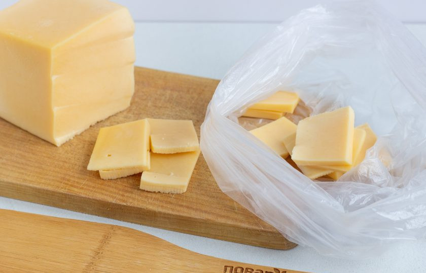 1. Этап. Салат Новогодний подарочек: Весь сыр нарежьте тонкими небольшими пластинами и сложите в целый чистый пакет. Завяжите пакет сверху и опустите в кипящую воду, чтобы вода полностью покрывала сыр. Держите пакет с сыром в кипящей воде 5-6 минут, пока сыр не расплавится. Можно придерживать пакет лопаткой, чтобы не всплывал.