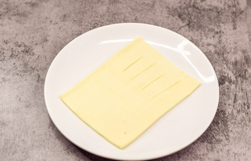 1. Этап. Слойки с ежевикой: Слоеное тесто раскатайте немного и нарежьте на 4 прямоугольника. Визуально разделите прямоугольник на две половины. На одной половине теста сделайте небольшие надрезы.