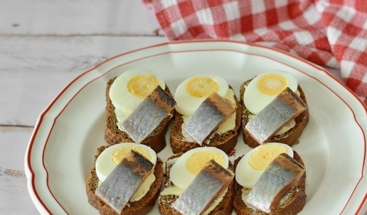 1. Этап. Бутерброды с селёдкой и яйцом: Выложите на них нарезанные яйца. Берите красивые центральные части яйца, где срез желтка виден хорошо. Остающиеся краешки яиц используйте в других блюдах, например в салатах. Сверху выложите ломтики селёдки, стараясь не закрыть желток.