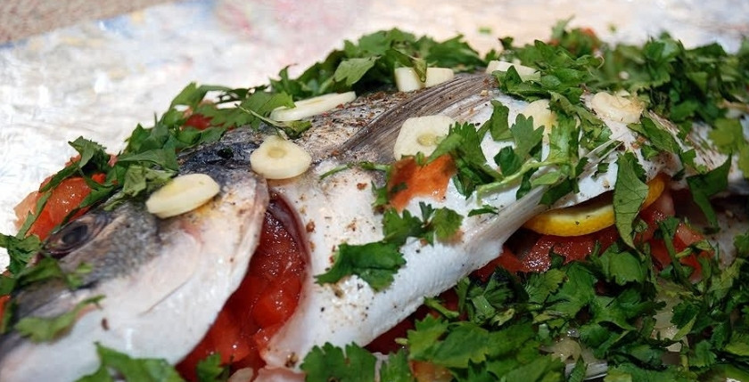 1. Этап. Дорада в фольге: 5. Рыбу, нафаршированную жареным луком и помидорами, переложите на фольгу. Очистите чеснок и порежьте тонкими пластинами. Спинку и бока дорады промажьте оливковым маслом. Затем разложите по всей длине тушки чеснок. Пересыпьте зеленью (петрушка или кинза). Полейте столовой ложкой лимонного сока.