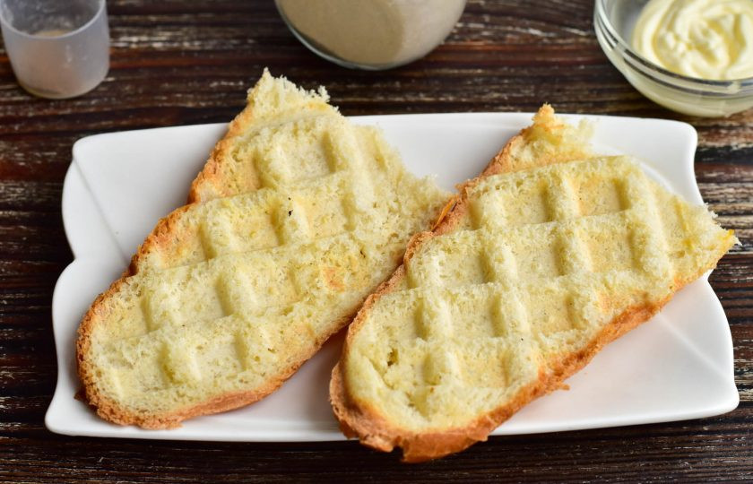 1. Этап. Голландские бутерброды с селедкой на багете: Минибагет разрежьте пополам, а затем вдоль пополам. Обжарьте его в вафельнице или на сковороде.