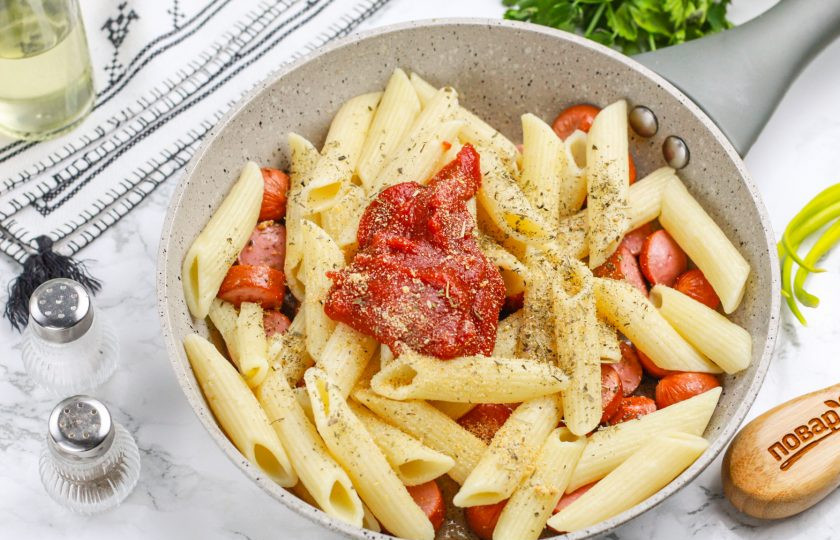 1. Этап. Макароны с сосисками на сковороде: Добавьте томатную пасту, сушеный молотый чеснок и базилик, аккуратно все перемешайте. По желанию можно добавить и другие специи, пряности.