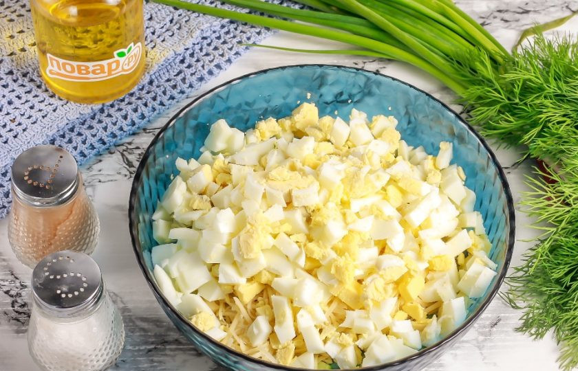1. Этап. Салат с яйцом, огурцом, зелёным луком и сыром: Очистите отварные куриные яйца от скорлупы, промойте в воде и нарежьте кубиками. Добавьте в емкость.