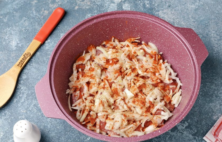 1. Этап. Мясо с квашеной капустой по-немецки: Сверху на мясо выложите нарезанный перьями лук. Посыпьте всё солью и специями.