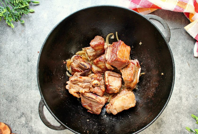 1. Этап. Говяжьи ребрышки в казане с луком: Верните в казан обжаренные ребрышки, посолите, поперчите и перемешайте, обжарьте еще одну минуту.