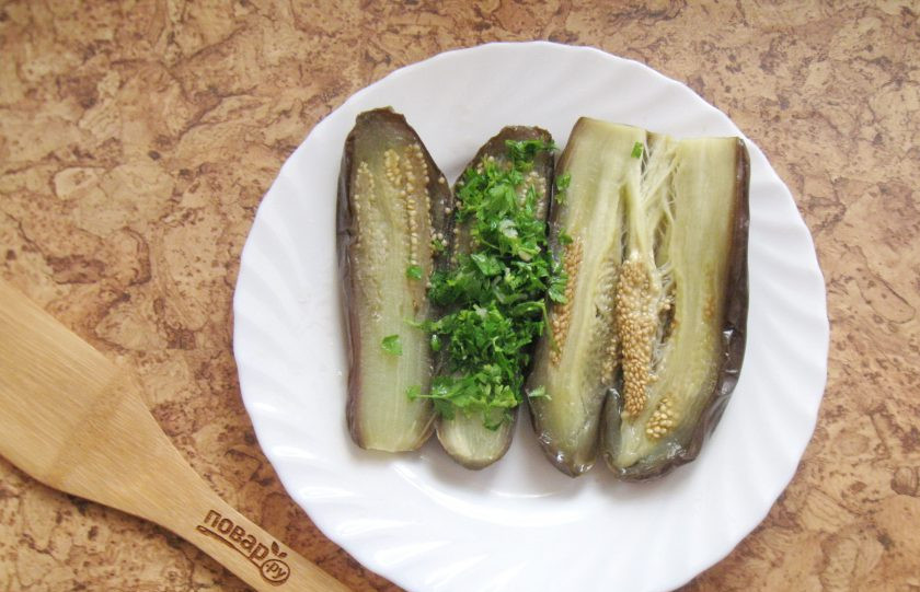 1. Этап. Квашеные фаршированные баклажаны: На одну сторону разрезанного баклажана выложите начинку из петрушки и чеснока. Соедините обе половинки баклажана.