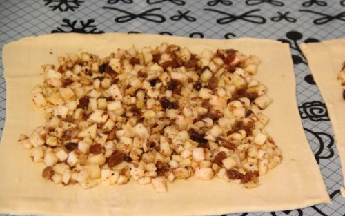 1. Этап. Яблочный штрудель простой: Аккуратно выложите начинку на тесто, распределяя ее по всей поверхности равномерно. Посыпьте яблоки, изюм и орехи сахаром. Также можно добавить немного ванилина или корицы для аромата.