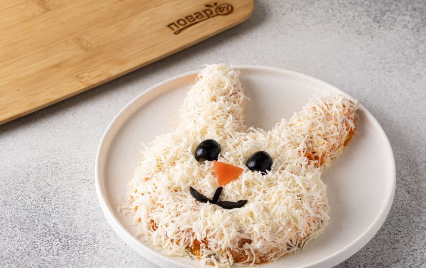 1. Этап. Вегетарианский салат в виде Кролика на Новый год 2023: Сделайте из маслин глаза и рот кролика, а из кусочка помидора треугольный носик. Накройте салат защитным колпаком и уберите на пару часов в холодильник пропитаться.