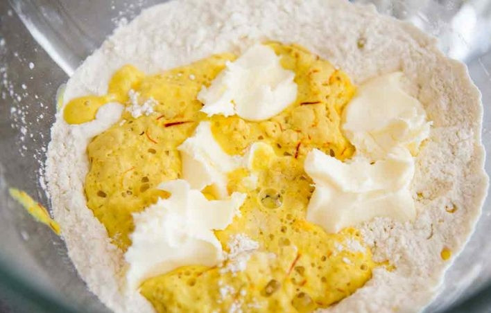 1. Этап. Булочки с шафраном: 4. В центре мучной смеси сделайте углубление, влейте молоко, добавьте яйца (2 штуки), сметану и сливочное масло.