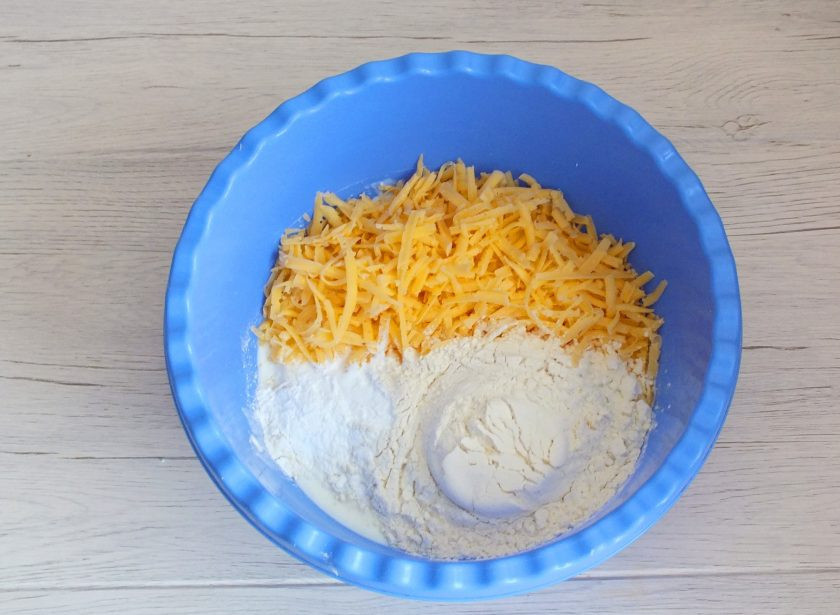 1. Этап. Творожное печенье с сыром: Натрите на крупной терке сыр, переложите в чашу. Добавьте 2 стакана муки, разрыхлитель.