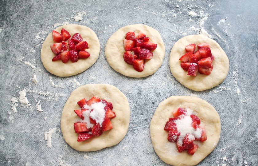 1. Этап. Пирожки с клубникой из дрожжевого теста в духовке: Переложите тесто на стол посыпанный мукой и разделите его на кусочки и сформируйте шарики. Накройте их и дайте постоять 15 минут. Из шариков сформируйте лепешки, разложите начинку и посыпьте сахаром.