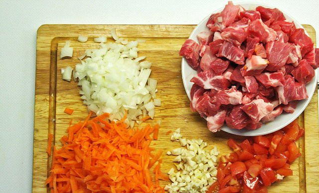 1. Этап. Cолянка тушеная: Помойте и почистите все остальные овощи и мясо. У помидоров снимите шкурку. Измельчите чеснок, лук и томаты. Морковь натрите на тёрке. Мясо нарежьте крупными кусочками.