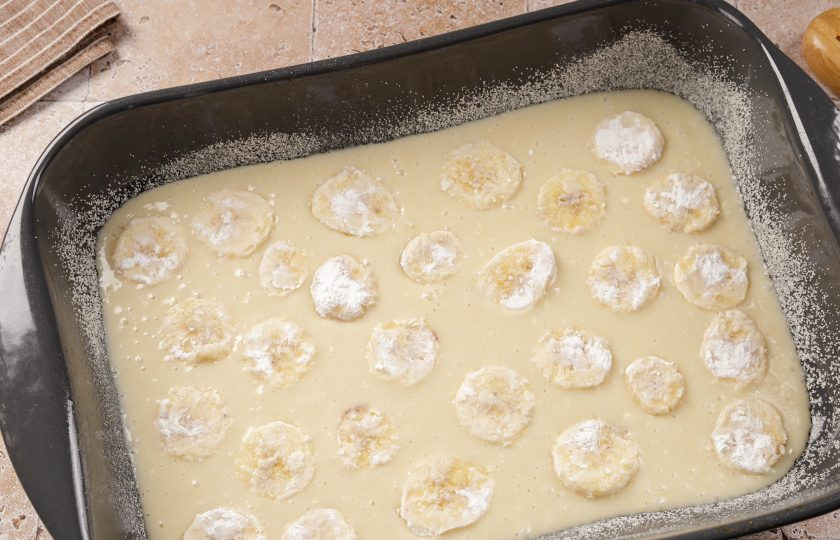 1. Этап. Заливной пирог с бананами: Жаропрочную форму смажьте маслом. Дно и бока обсыпьте мукой или манкой. Вылейте половину порции теста. Сверху распределите нарезанные бананы.