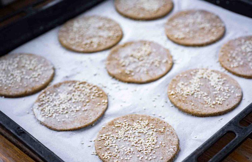 1. Этап. Ржаные лепешки на кефире: Круглой вырубкой вырежете заготовки лепешек и переложите каждую на противень, застеленный пергаментом для выпекания. Смажьте каждую заготовку теплой водой и присыпьте кунжутом. Отправьте выпекаться в уже разогретую до 180 градусов духовку на 10 минут.