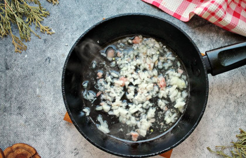 1. Этап. Кукурузная каша с тушенкой: В сковороду с толстым дном выложите жир из тушенки или влейте растительное масло. Репчатый лук мелко порежьте и выложите в сковороду. Обжаривайте на среднем огне в течение 2-3 минут.