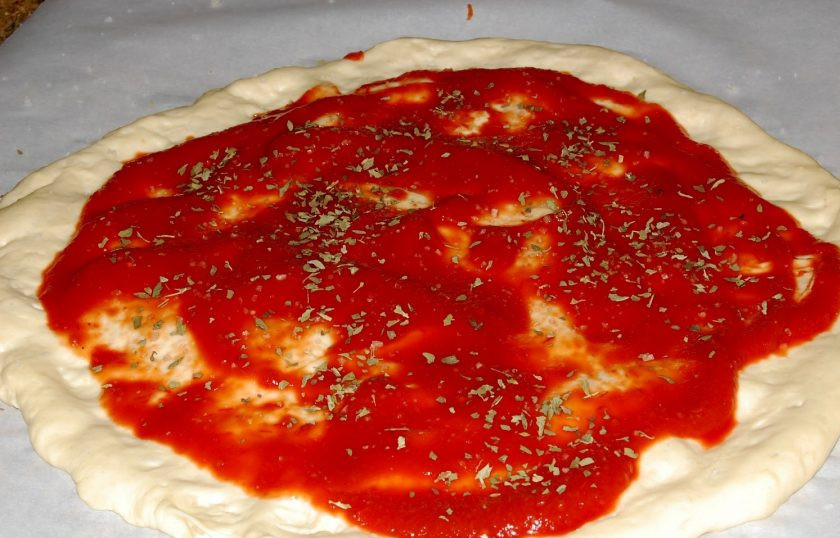 1. Этап. Сырная пицца Четыре сезона: 4. Смажьте основу для пиццы томатным соусом, добавьте базилик и орегано, посолите.