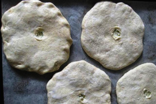 1. Этап. Осетинский пирог в духовке: Застелите противень пергаментом, выложите на него наши колобки швом вниз и аккуратно расплющите их ладонью до плоского состояния. Сверху вделайте небольшие дырочки для выхода пара, а также смажьте кефиром.