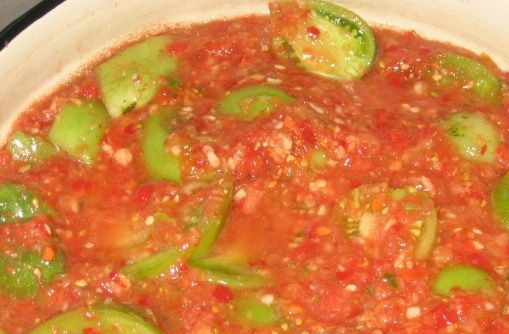 1. Этап. Аджика из зеленых помидоров сырая: Зелёные помидоры помойте и нарежьте четвертинками или половинками. Смешайте их с заготовкой из предыдущего шага и поставьте на огонь до закипания, потом, помешивая, тушите 20 минут.